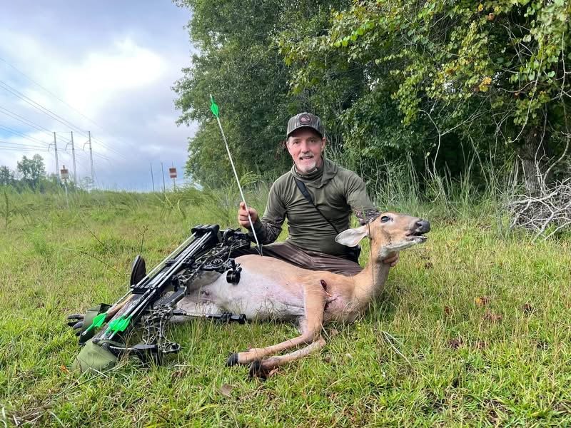 Hunter kneeling with a whitetail doe, white arrow in hand and crossbow at his side