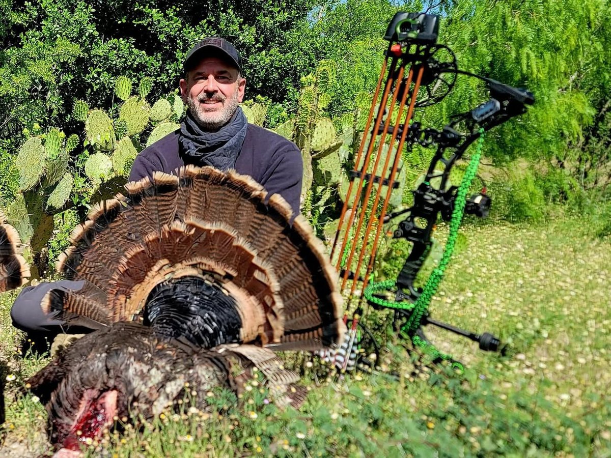 Hunter with a spring gobbler fanned out, compound bow and arrows in cactus country