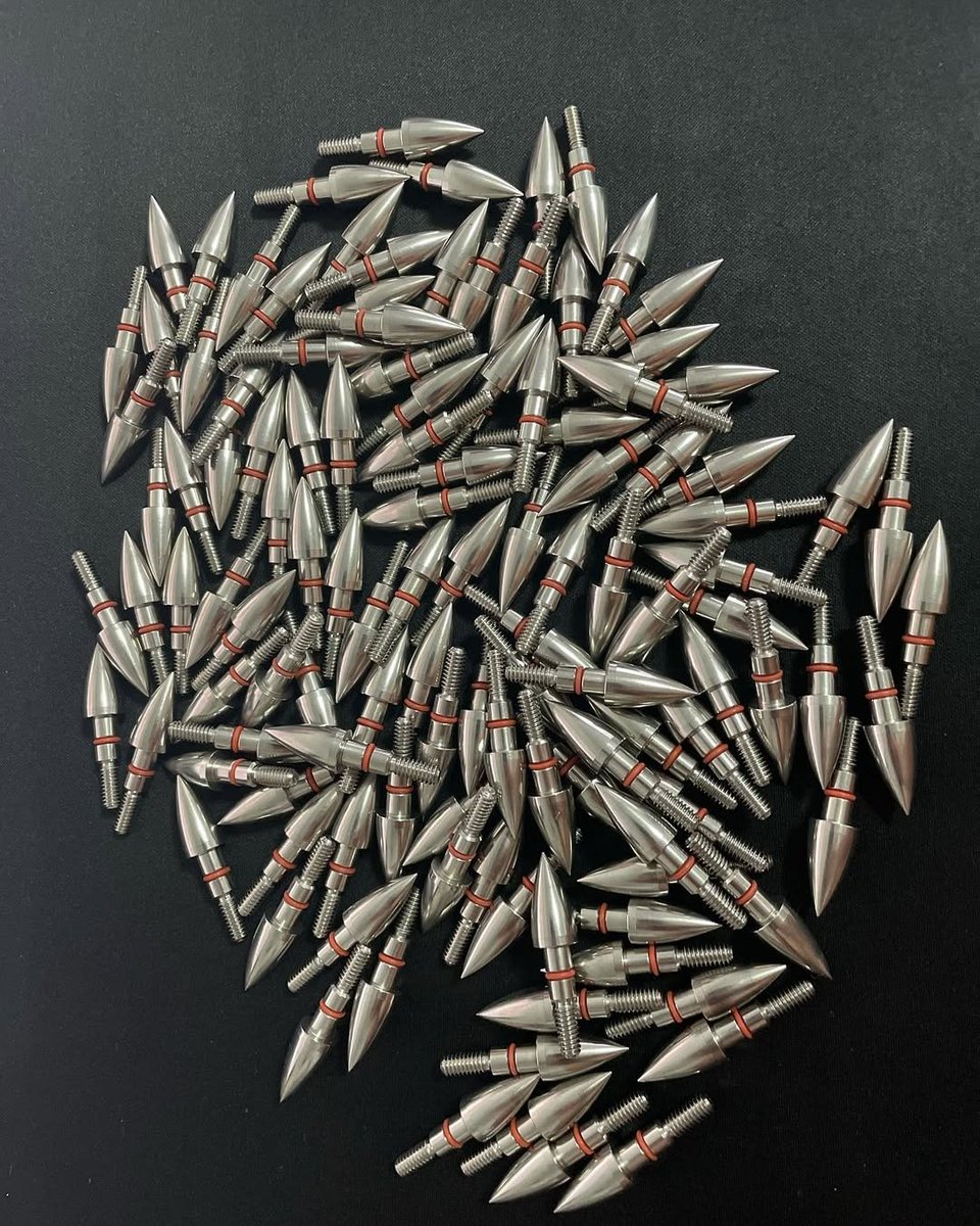 Pile of machined screw-in field points with O-ring seals on black velvet